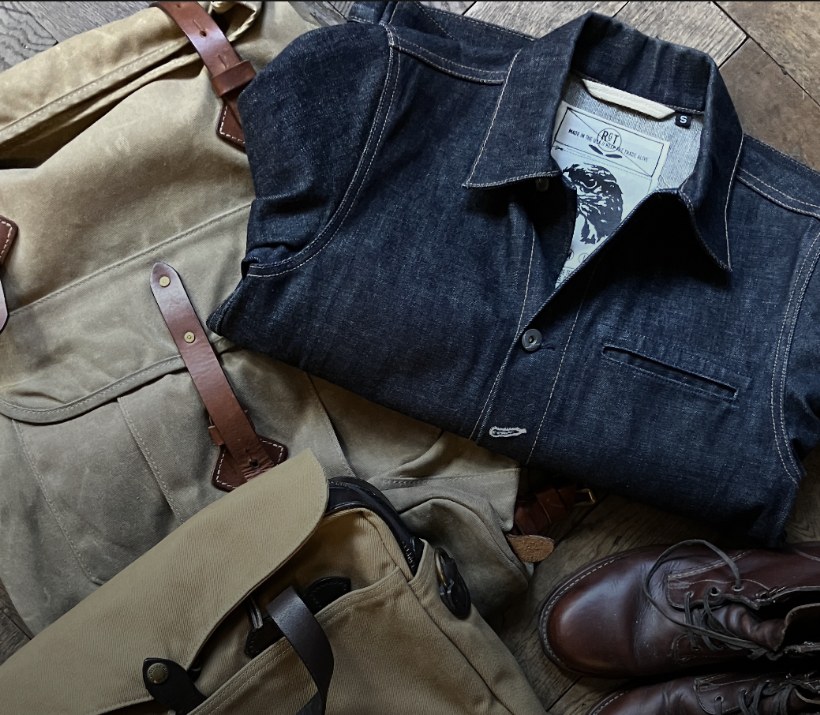 Vintage-Jeansjacke, gewachste Canvas-Tasche und Stiefel auf Fischgrätparkett